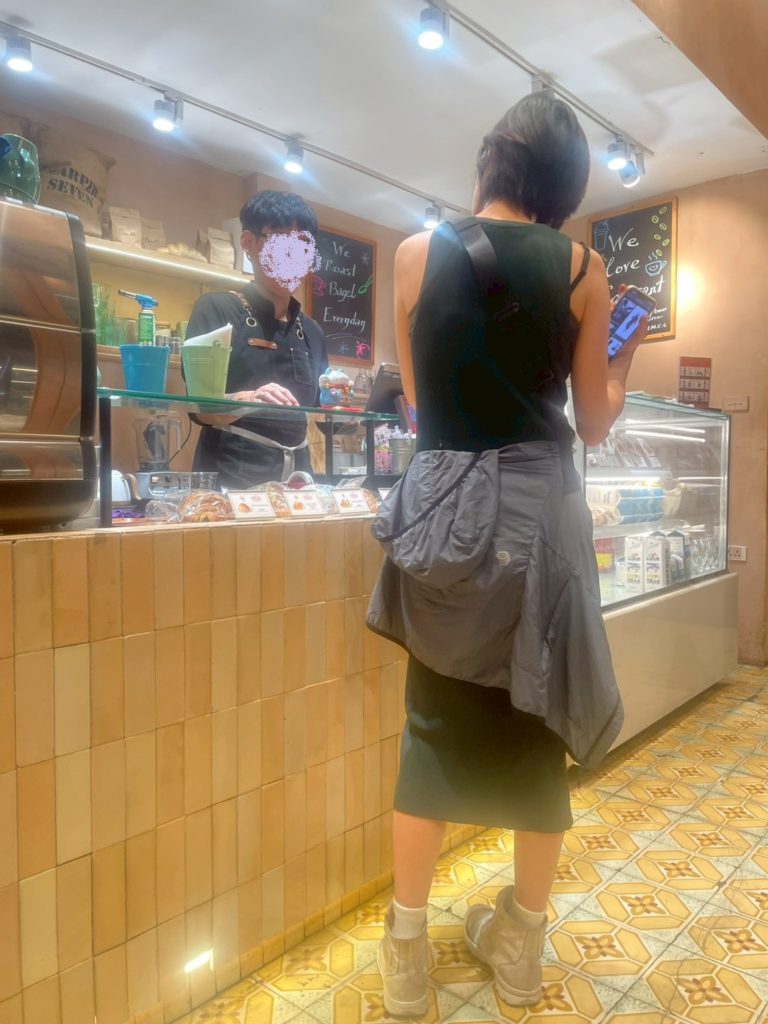 ハノイ市内のカフェのカウンターで注文中の女性と店員。ガラスケースとメニュー看板が見える。