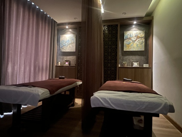 ハノイのスパで、2台のマッサージベッドが並ぶ落ち着いた室内。壁に絵画が飾られ、暖色の照明が照らしている。