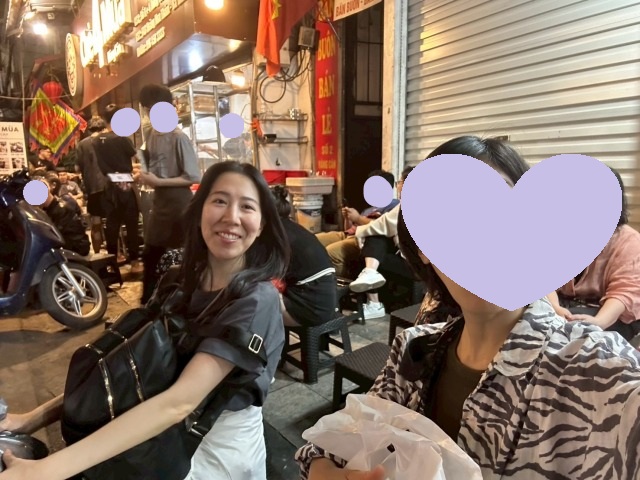 ハノイのチェー店「Chè 4 Mùa」の路上席で、訪問者がチェーを楽しんでいる様子。背景に店の外観と客のにぎわいが写っている。