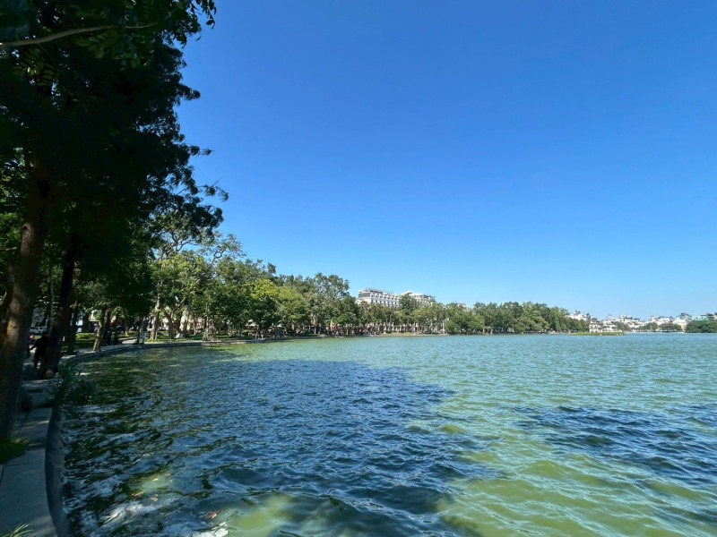 青空の下に広がるハノイのホアンキエム湖と湖畔の木々の風景